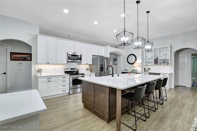 kitchen with an island with sink, appliances with stainless steel finishes, decorative light fixtures, light hardwood / wood-style floors, and white cabinetry