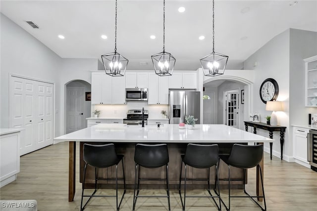 kitchen featuring appliances with stainless steel finishes, a center island with sink, light hardwood / wood-style flooring, and decorative light fixtures