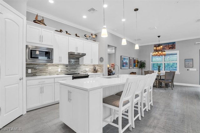 kitchen with sink, stainless steel appliances, pendant lighting, a kitchen island with sink, and white cabinets