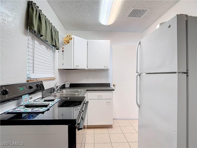 kitchen featuring visible vents, white cabinets, dark countertops, freestanding refrigerator, and a sink