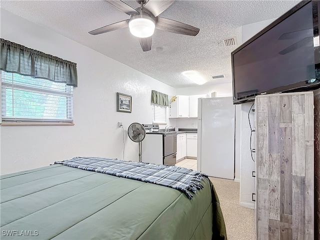 bedroom with light carpet, visible vents, a ceiling fan, freestanding refrigerator, and a textured ceiling