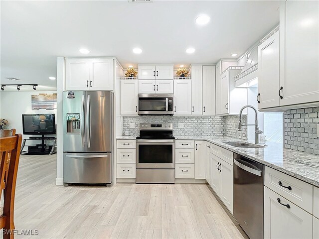 kitchen with light stone countertops, white cabinetry, appliances with stainless steel finishes, and a sink