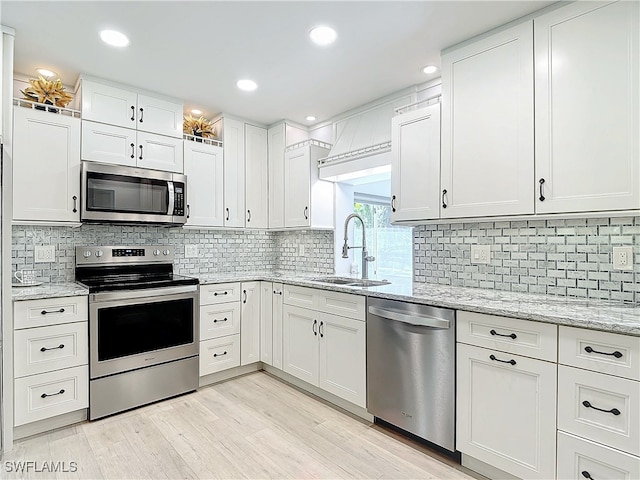 kitchen featuring stainless steel appliances, a sink, white cabinetry, and light stone countertops