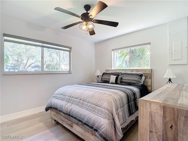 bedroom featuring ceiling fan, electric panel, baseboards, and wood finished floors