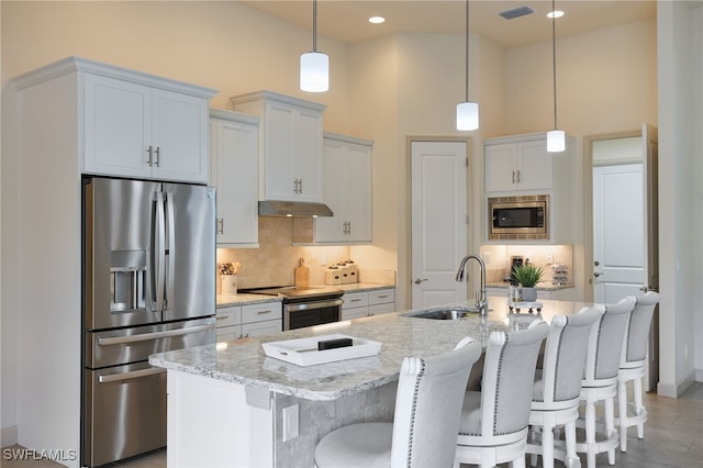 kitchen with a kitchen island with sink, sink, light stone countertops, white cabinetry, and stainless steel appliances