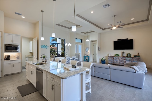 kitchen with white cabinets, an island with sink, appliances with stainless steel finishes, a tray ceiling, and a breakfast bar area