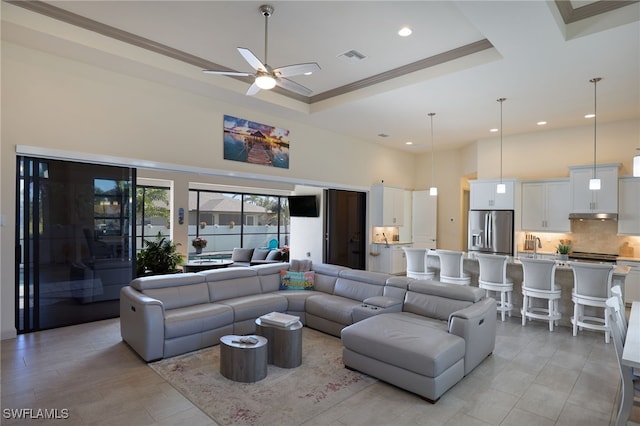 living room with a tray ceiling, ceiling fan, a high ceiling, and ornamental molding