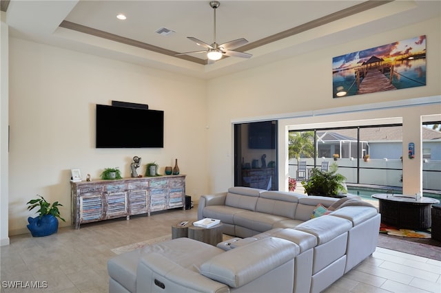 living room featuring a raised ceiling, ceiling fan, and ornamental molding