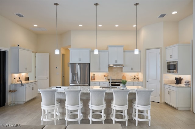 kitchen with pendant lighting, stainless steel appliances, white cabinetry, and a high ceiling