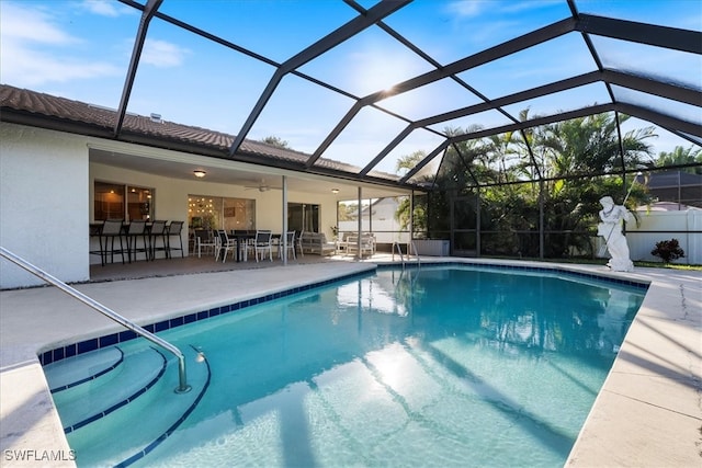 view of pool featuring glass enclosure, ceiling fan, a patio area, and an outdoor bar