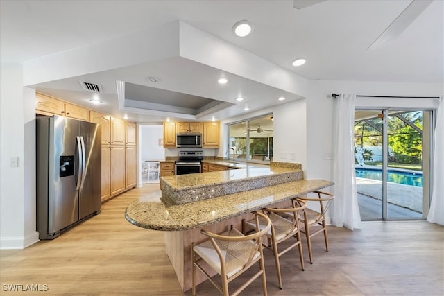 kitchen featuring light stone countertops, light hardwood / wood-style flooring, kitchen peninsula, a breakfast bar, and appliances with stainless steel finishes