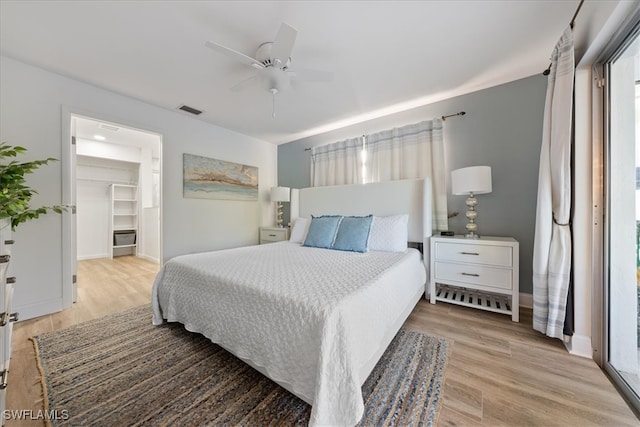 bedroom featuring a closet, a walk in closet, light hardwood / wood-style floors, and ceiling fan