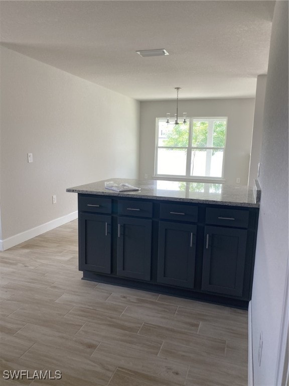 kitchen featuring light stone counters, pendant lighting, light wood-type flooring, and a notable chandelier