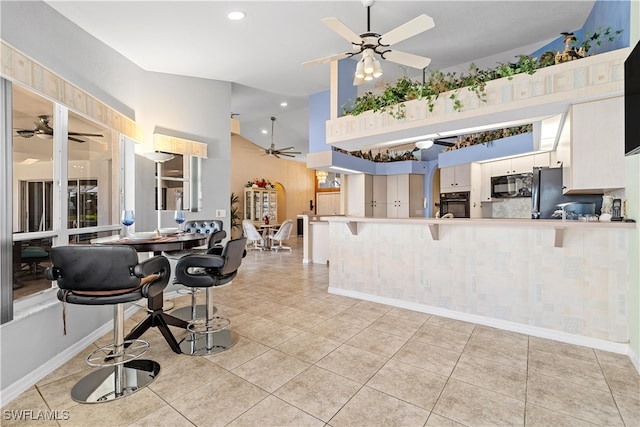 kitchen featuring kitchen peninsula, black appliances, light tile patterned floors, white cabinetry, and a breakfast bar area