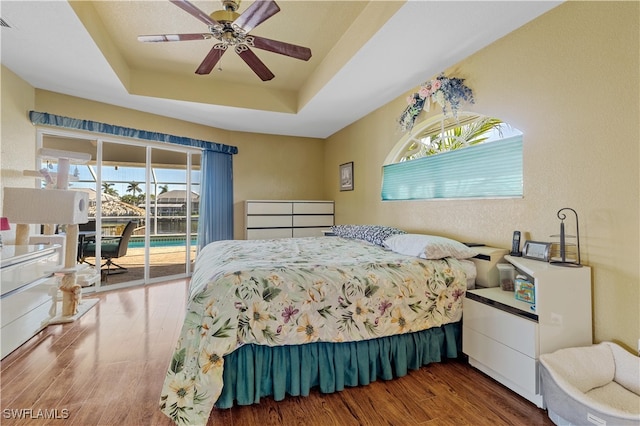 bedroom with a tray ceiling, access to exterior, ceiling fan, and hardwood / wood-style floors