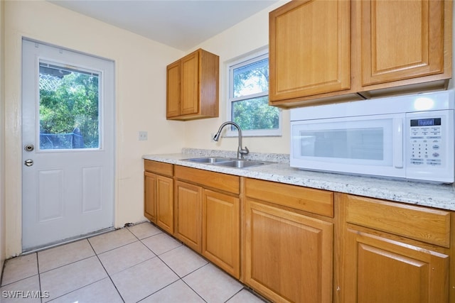 kitchen with plenty of natural light, light tile patterned flooring, light stone countertops, and sink