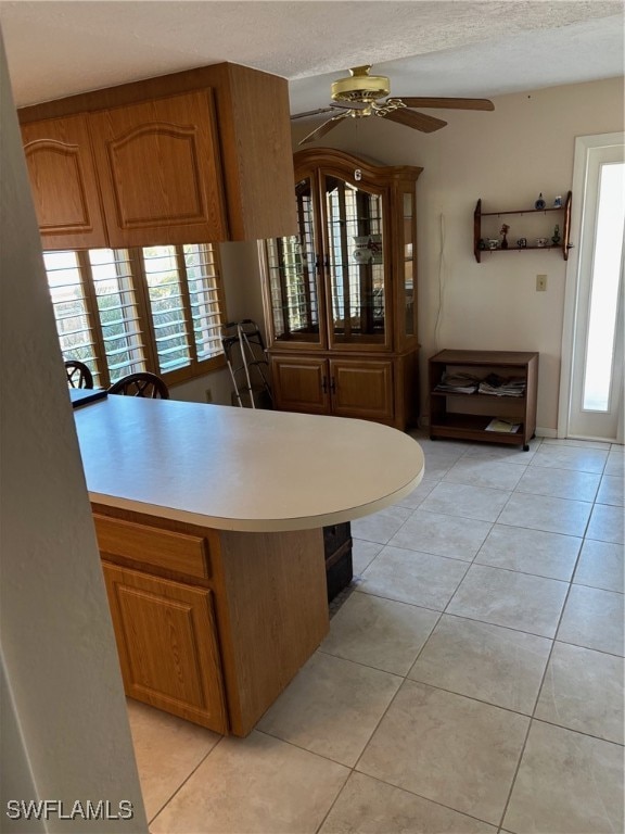 kitchen with kitchen peninsula, ceiling fan, light tile patterned floors, and a textured ceiling