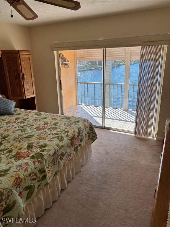 carpeted bedroom with access to exterior, a textured ceiling, a water view, and ceiling fan