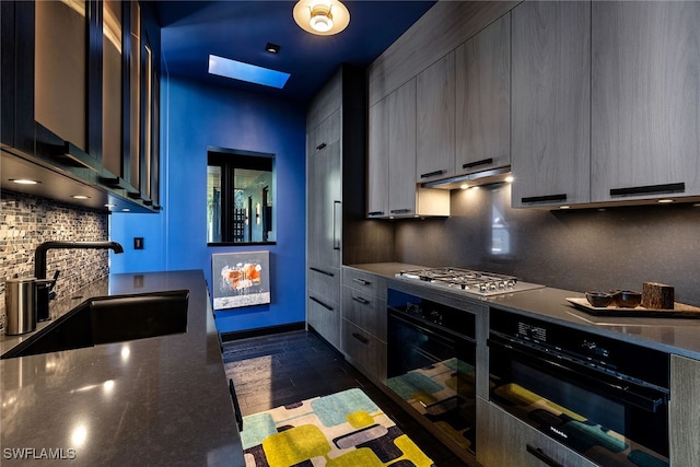 kitchen featuring a skylight, sink, stainless steel gas cooktop, dark hardwood / wood-style flooring, and backsplash