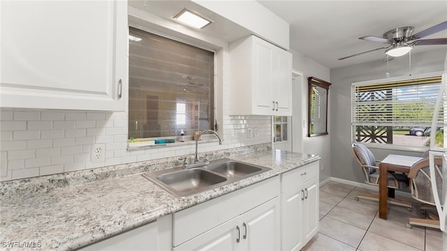 kitchen featuring backsplash, sink, light stone countertops, light tile patterned floors, and white cabinetry