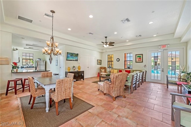 dining room with ceiling fan with notable chandelier, a raised ceiling, and french doors