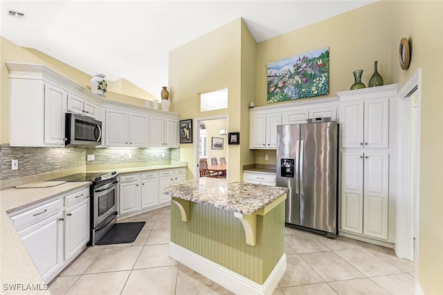 kitchen with a breakfast bar area, light tile patterned flooring, light stone counters, white cabinetry, and stainless steel appliances