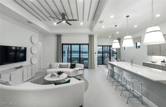 living room featuring a raised ceiling, ceiling fan, sink, and crown molding