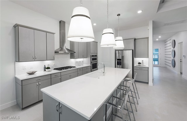 kitchen with sink, an island with sink, gray cabinets, and wall chimney range hood