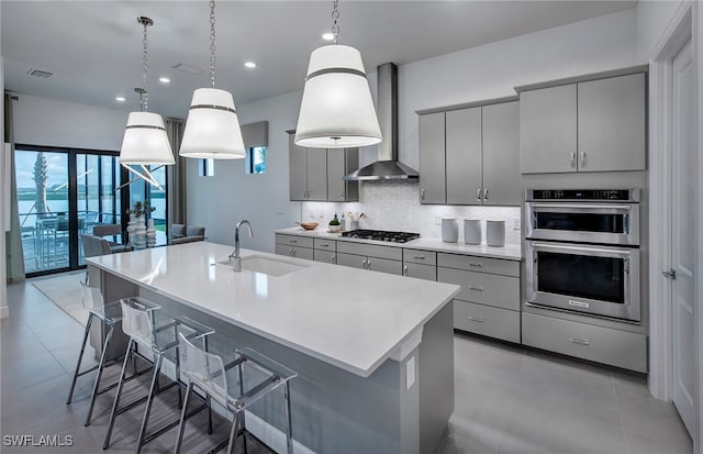 kitchen with gray cabinetry, a breakfast bar, pendant lighting, sink, and wall chimney exhaust hood