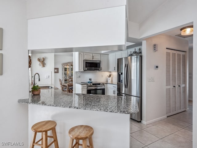 kitchen featuring light stone countertops, sink, stainless steel appliances, kitchen peninsula, and a breakfast bar area