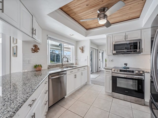 kitchen featuring light stone countertops, sink, a raised ceiling, white cabinets, and appliances with stainless steel finishes