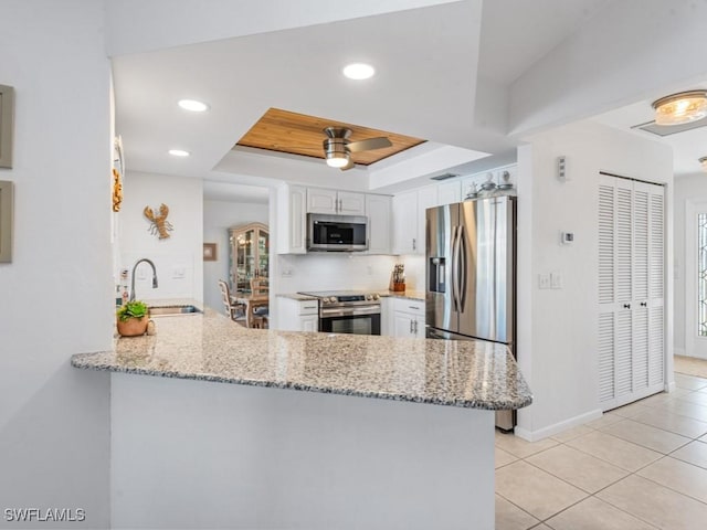 kitchen with a peninsula, a sink, appliances with stainless steel finishes, white cabinetry, and a raised ceiling