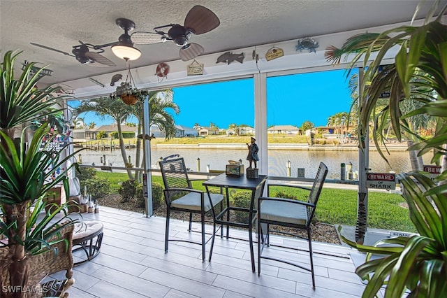 sunroom / solarium featuring ceiling fan and a water view