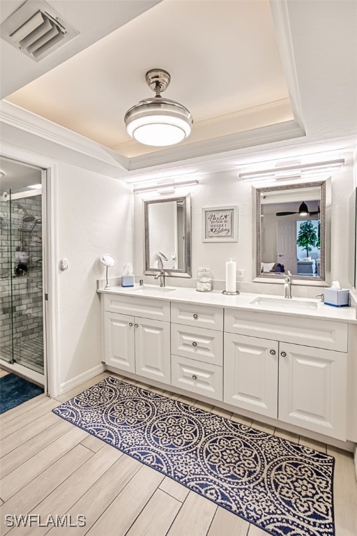 bathroom featuring an enclosed shower, vanity, a tray ceiling, crown molding, and wood-type flooring