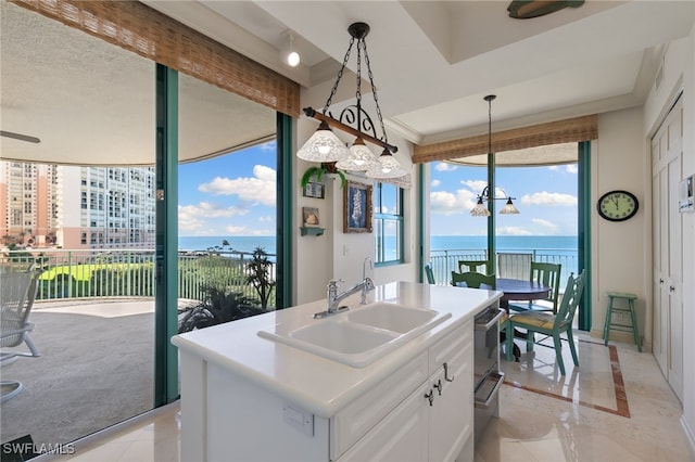 kitchen featuring sink, hanging light fixtures, white cabinets, an island with sink, and a water view