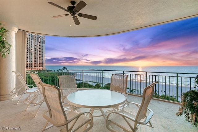 balcony at dusk with ceiling fan and a water view