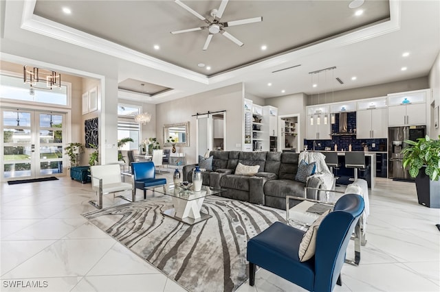 living room featuring ceiling fan with notable chandelier, a towering ceiling, a barn door, and a tray ceiling