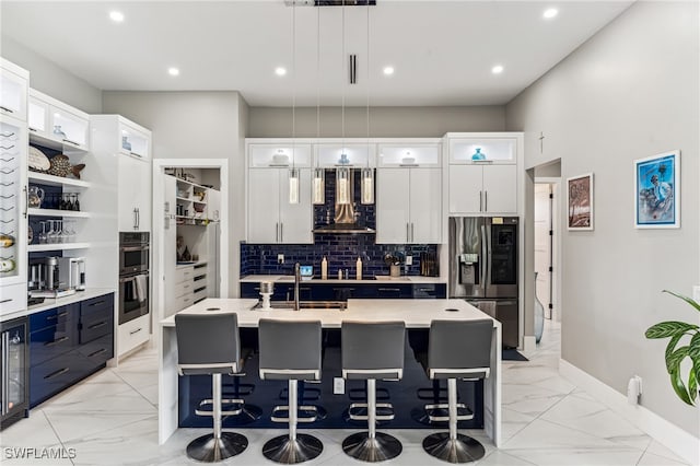 kitchen with white cabinetry, extractor fan, decorative light fixtures, a center island with sink, and appliances with stainless steel finishes