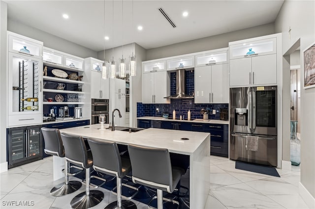 kitchen with a kitchen island with sink, wall chimney range hood, a breakfast bar area, white cabinetry, and stainless steel appliances