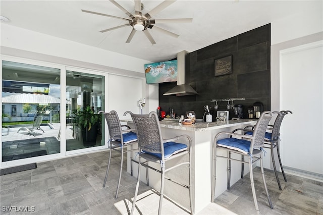 kitchen featuring wall chimney exhaust hood, kitchen peninsula, a breakfast bar, and tasteful backsplash