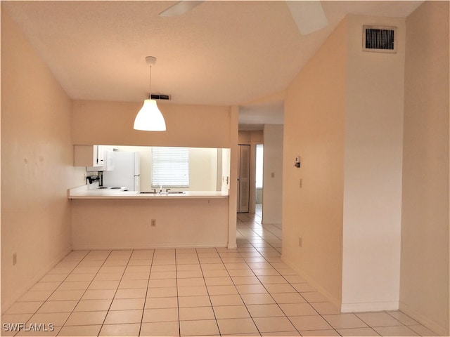 kitchen with sink, kitchen peninsula, white fridge, decorative light fixtures, and light tile patterned floors