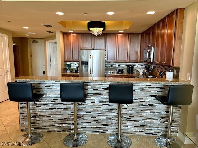 bar with light stone countertops, appliances with stainless steel finishes, tasteful backsplash, and a tray ceiling