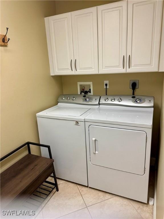 clothes washing area featuring washing machine and clothes dryer, light tile patterned floors, and cabinets