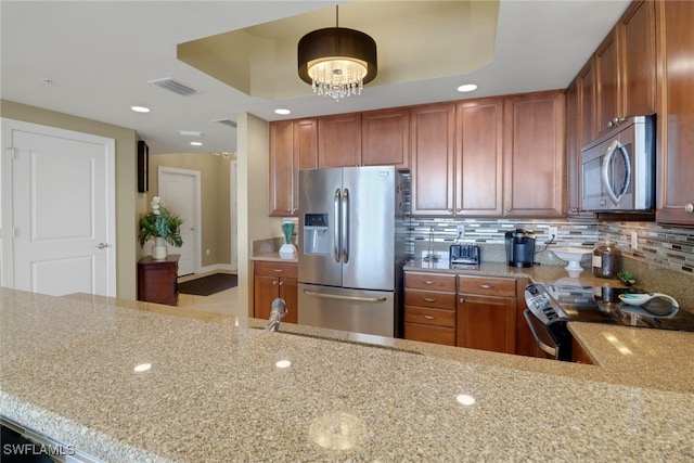 kitchen featuring visible vents, stainless steel appliances, decorative backsplash, a raised ceiling, and brown cabinets