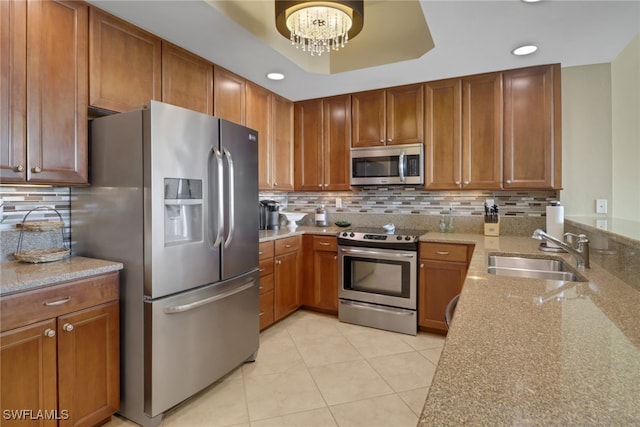 kitchen featuring light stone countertops, a sink, stainless steel appliances, a notable chandelier, and backsplash