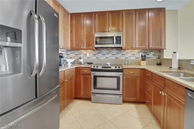 kitchen featuring backsplash, light stone countertops, stainless steel appliances, and a sink