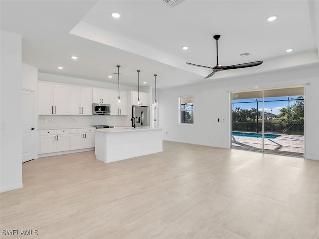 kitchen featuring ceiling fan, stainless steel appliances, an island with sink, pendant lighting, and white cabinets