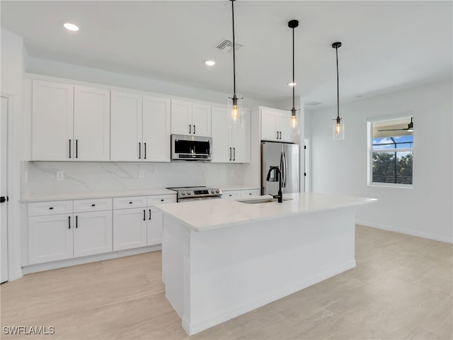 kitchen with white cabinets, decorative light fixtures, stainless steel appliances, and a kitchen island with sink