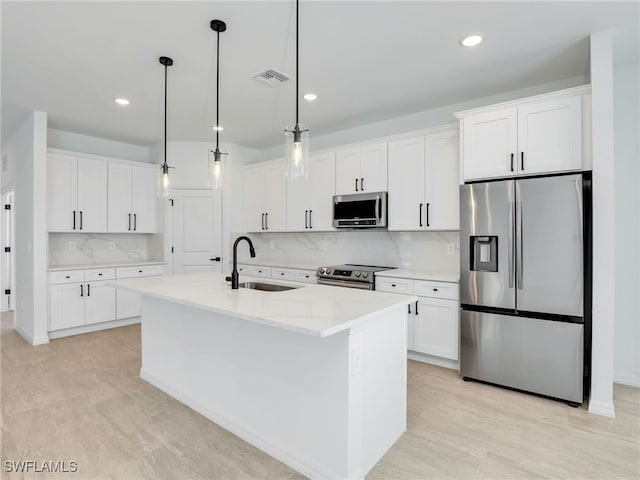 kitchen featuring appliances with stainless steel finishes, sink, decorative light fixtures, white cabinetry, and an island with sink