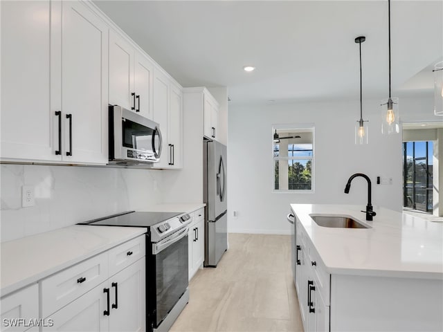 kitchen with a center island with sink, sink, decorative light fixtures, white cabinetry, and stainless steel appliances